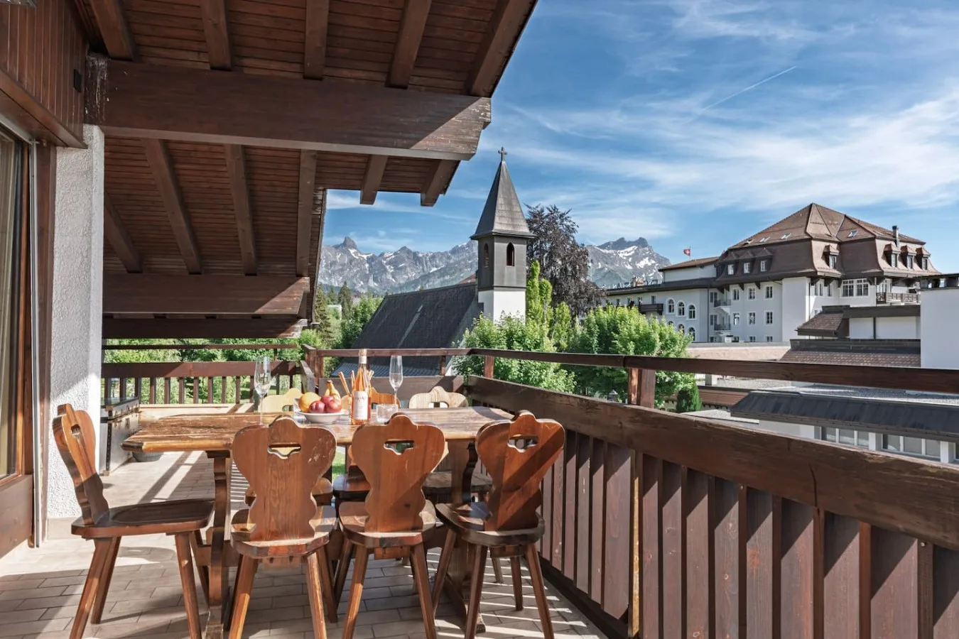 Large covered balcony of the penthouse with wooden table and view of the church tower and the Alps, Villars-sur-Ollon